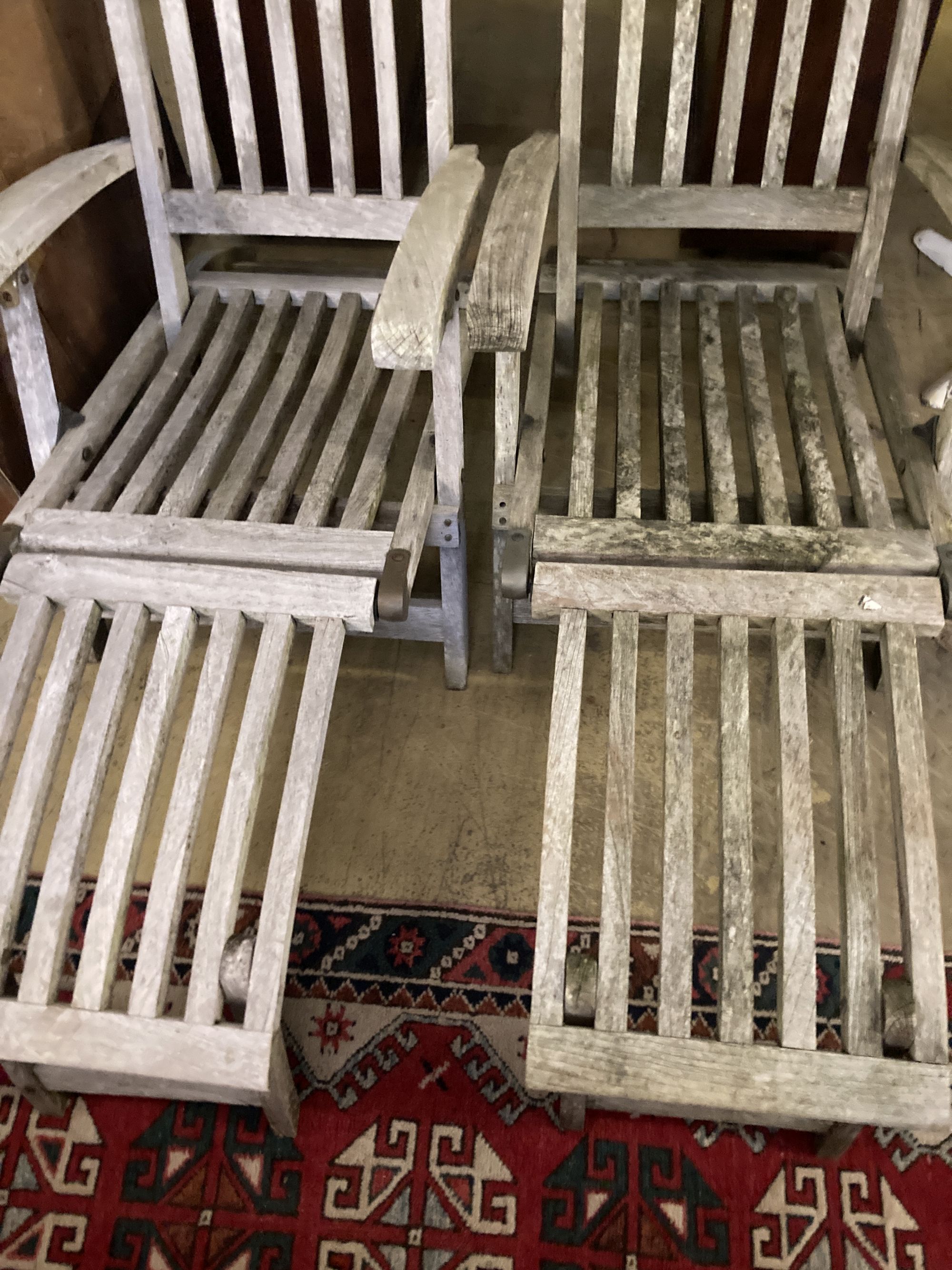 A pair of weathered teak steamer garden chairs with cushions